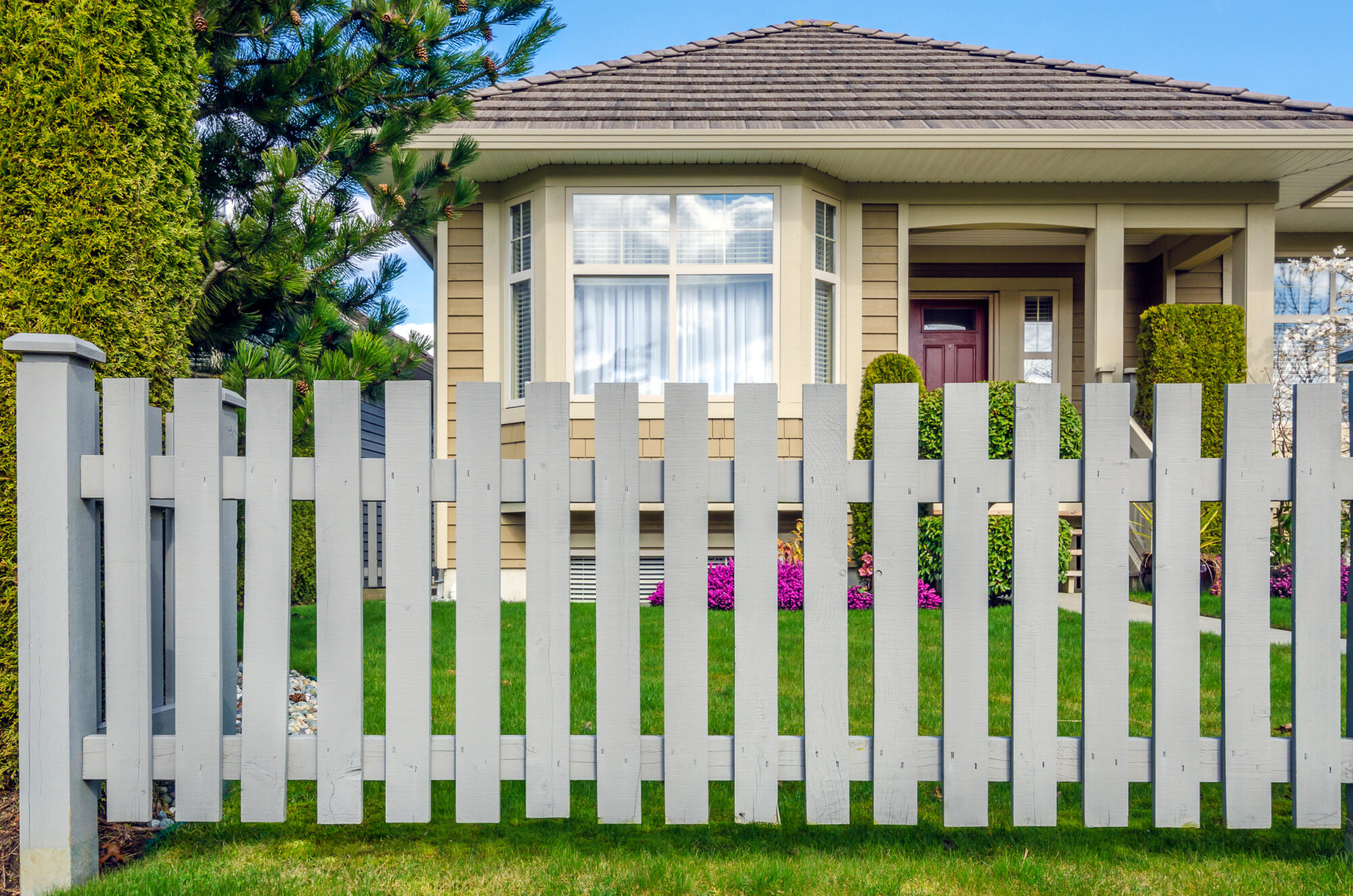 new gray picket fence outside of beautiful suburban home with landscaped lawn